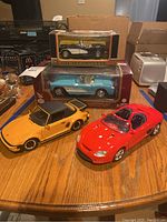 Four model cars on wooden table: two in original boxes (black and blue 1959-57 Chevrolet Corvettes), two loose (yellow and red convertibles).