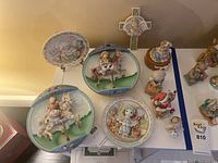 Group view of two Bradford Exchange music plates, Cherished Teddies figurines, and a decorative cross on a white surface.