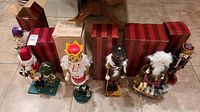 Five nutcracker figurines alongside their original striped red and brown boxes on a tiled floor.