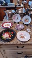 Four decorative Crown Ducal plates and one metal serving tray displayed on countertop. Plates have maroon borders and fruit designs.