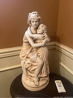 Front side view of statue showing woman and child embracing, seated on rounded base.