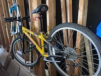 Full view of yellow Norco Hornet bicycle leaning against a wooden frame wall, showing entire bike including tires, seat, and handlebars.