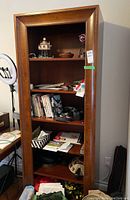 Front view of the tall wooden bookcase filled with various books, papers, and decorative objects across six shelves.