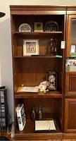 Front view of wood bookcase showing four shelves with various items on them, signs of finish flaws visible on shelf edges