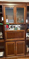 Front view of the wooden bookcase showing two upper glass front doors revealing shelves inside, a pulldown front bar section in the middle and two wood cupboard doors below.