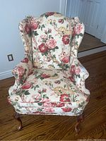 Front view of the upholstered wing back chair showing floral fabric upholstery and wood cabriole legs on hardwood floor.
