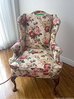 Frontal view of floral wing back chair showing detailed upholstery and wooden legs.