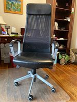 Front view of IKEA Markus office chair showing leather seat and mesh backrest with metal armrests and base with caster wheels.