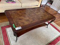 Front angled view of the two-tier coffee table showing the inlaid wood top, curved metal legs, and lower shelf