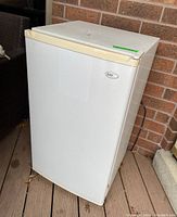 White Sanyo mini fridge model SR-3620W with slightly yellowed top and handle, shown at an angle on a deck against a brick wall.