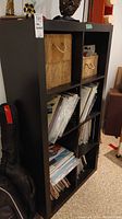Black laminate Ikea shelving unit with 8 compartments, top row has two woven baskets, filled with records in multiple compartments.