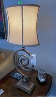 Lamp with beige fabric shade and metal/plastic spiral base on side table with lamp tag 647.