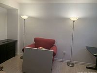 Two tall metal pole lamps with frosted glass bowl shades, positioned behind a red armchair in a living room setting.
