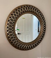 Full front view of the circular mirror mounted on the wall showing wood frame with woven lattice pattern.