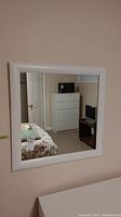 Mirror hung on wall reflecting a dresser, a door, and part of a bedroom.