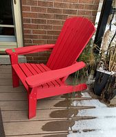 Side angles of a single red Adirondack style wooden outdoor armchair showing the slatted backrest, seat, and wide armrests.