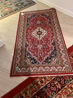 Full top view of the red patterned area rug with tags attached, showing the detailed design and colors.