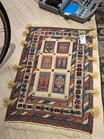 Photo of decorative area rug with central medallion pattern, fringed tassels, and multicolor border on light flooring.