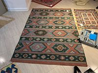 Overall view of the rectangular patterned area rug laid on a light tile floor showing the geometric designs and colors.