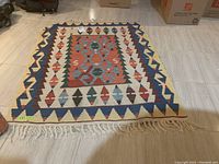 Rectangular rug laid on a tiled floor showing the full geometric pattern and fringed edges, photo taken to display item front.