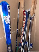 Three pairs of skis, two ski poles and one hockey stick leaning against wall