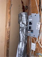 Pair of waxless skis with poles wrapped in silver protective cover adjacent to electrical panel in basement