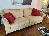 Front angled view of the beige fabric sofa showing right arm damage and two red accent cushions