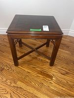 Full view of small wooden end table with decorative carved wood supports and crossbar stretcher under the top.