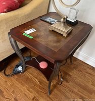 Side view of the wood side table showing inlaid top, curved metallic legs, and lower shelf with some electric cords underneath.