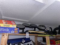 Top shelf view showing toy electronic drum set, toy guitar, and puzzle boxes including Labyrinth game.