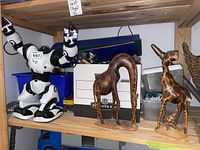 Black and white plastic robot and two wooden giraffe figurines on wooden shelf.