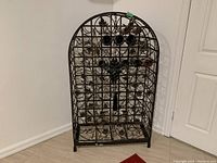 Front view of decorative metal wine rack with locking doors and floral metalwork design. Shows bottles on some shelves.