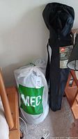 MEC down sleeping bag and Ozark Trail Deluxe Arm Chair in black carrying bag leaning against wall.