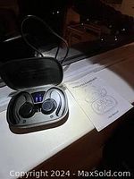 Silver/grey wireless earbuds in an open charging case with blue LED display and instruction manual beside it.