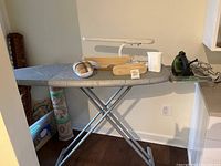 Ironing board set up with lamp, various pressing arms on top, Rowenta iron present