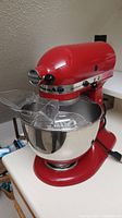 Front-left view of cherry red mixer with bowl and clear plastic pour shield