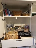 Open cabinet showing shelf and open drawer with books, baskets, yarn bins, and needle cases.