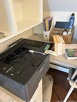 Brother laser printer on desk with cords and instruction manual visible
