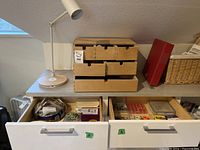 The white adjustable desk lamp on top of a wooden dresser with a multi-drawer organizer and sewing items in open drawers below.