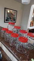 All eight clear plastic storage jars with varied sizes and bright red lids shown on a kitchen countertop