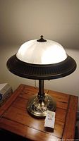 Front view of lit table lamp showing white frosted glass dome shade with metal body and base.