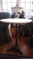 Full view of accent table with cast metal base and round stone top, positioned between armchairs with a large stuffed panda behind.