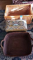 A view from above showing the light brown wicker basket, Oracle wood chest with decorative inlay, and the dark brown woven basket with handles.