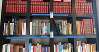 Wide view of bookshelf with multiple rows of hardcover books, mainly red volumes on top and assorted colors below including books on history, literature, and poetry.