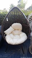 Front view of brown woven wicker egg chair with cream cushion and bolster