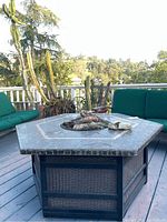 Front view of hexagonal stone top fire table on deck with faux logs