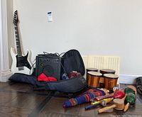 Overview of electric guitar in gig bag, amplifier, kids bongos and assorted percussion on floor
