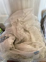 White lightweight parachute loosely folded on the floor against a wall, showing stitched lines down the fabric.