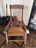 Front view of the vintage wooden rocking chair showing spindle back, armrests, and rush seat.