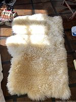 Full view of the cream-colored sheepskin rug laid out on a wooden floor, showing the overall size and shape.